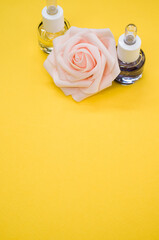 Poster - Vertical shot of essential oils next to a beautiful pink rose on a yellow surface