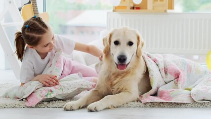 Wall Mural - Smiling little girl and calm dog lying on pillow under blanket in playroom