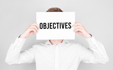Poster - man covers his face with a white paper with text objectives