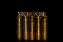 Violence Text Formed With Real Authentic Typeset Letters On Top Of Row Of 50 Cal BMG Rifle Bullet Casings Against Black Background