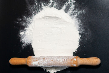 In the center of the screen on the table is a hill of white flour. There is a kitchen rolling pin at the bottom. 