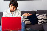 Fototapeta Na ścianę - Hispanic young man in casual clothes brainstorming at a distance with a laptop on a sofa with a calm and thoughtful attitude