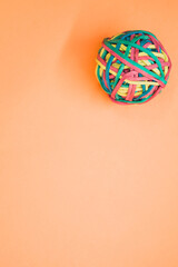 Vertical shot of a rubber ball made out of rubber bands isolated on an orange background