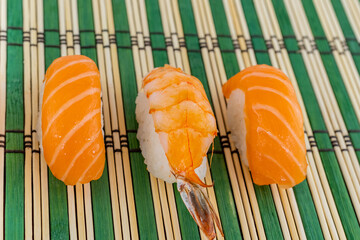 three sushi fresh salmon and traditional shrimp on a green background