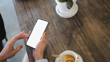 Mockup image of woman hands holding black mobile phone with blank white screen in cafe.