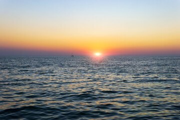 Wall Mural - Sailboat silhouetted against a colorful orange sunset sky in the open sea