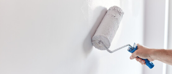 Male hand painting wall with paint roller. Painting apartment, renovating with white color paint