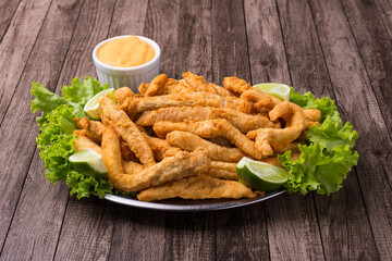 Gourmet photograph of portion and breaded fried fish served on lettuce leaves with lemons and tartar sauce to accompany.