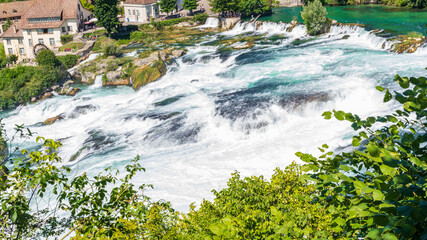 Wall Mural - Panorama des cascades du Rhin ou Rheinfall en Suisse par une journée ensoleillée avec un ciel bleu avec les rochers et un village en pose longue