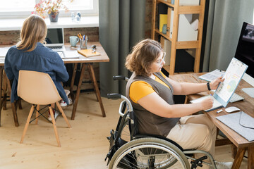 Young businesswoman in wheelchair looking at paper with charts and diagrams