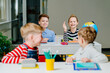 © Iryna - Four happy children in classroom. Smiling female pupil raised hand actively participate in the class of middle school.