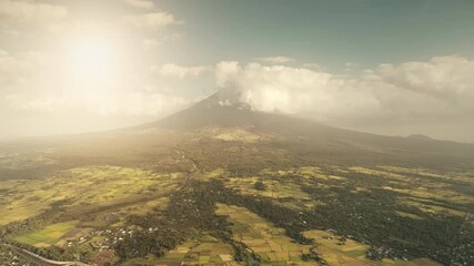 Wall Mural - Tropic sun farmlands at green volcano hillside valley aerial. Legazpi countryside at tropical Philippines with tourist attraction of Mayon mount. Clouds of haze eruption over mountain peak at sunlight