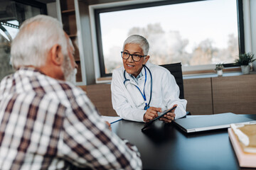 Wall Mural - Doctor and senior male patient discussing something while sitting at the table in the doctor's office. Medicine and healthcare concept.