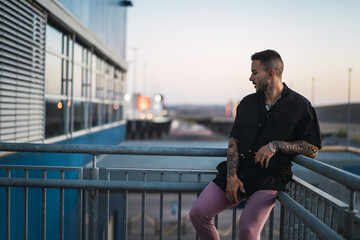 Wall Mural - Young hot man wearing a black oversize shirt and pink pants leaning on the handrails