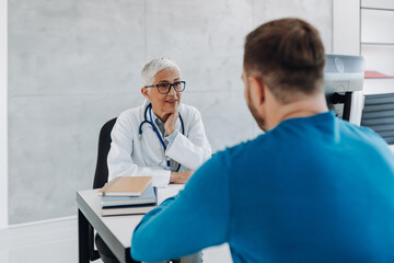 Wall Mural - Doctor and patient discussing something while sitting at the table in the doctor's office. Medicine and healthcare concept.