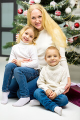 Cheerful Mom and her Cute Daughter and Son Sitting Next Christmas Tree.