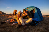 Fototapeta  - Happy group of friends camping and eating food at the sunset in the mountains.