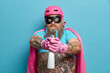 © wayhome.studio  - Serious self confident bearded male superhero holds cleaning detergnet and going to spray looks directly at camera wears prrotective helmet cloak mask going to tidy up everything poses indoor