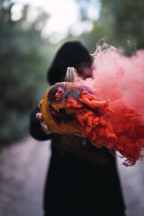 Wall Mural - Vertical shot of a man holding a carved pumpkin with red smoke - the concept of Halloween