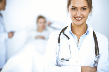 Wall Mural - Female doctor smiling on the background with patient in the bed and two doctors