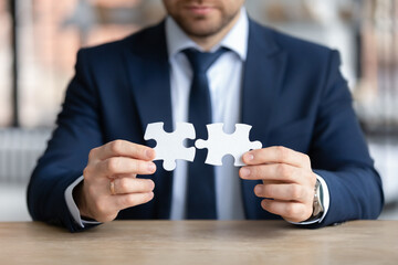 Close up focused young businessman putting puzzles together, finding difficult problem solution or involved in company growth strategy development, busy with brainstorming activity alone in office.