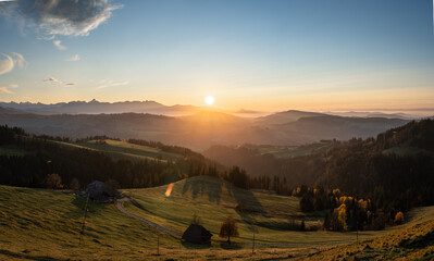 Wall Mural - overview swiss landscape with hills forests mountains in warm color during sunset or sunrise and epi