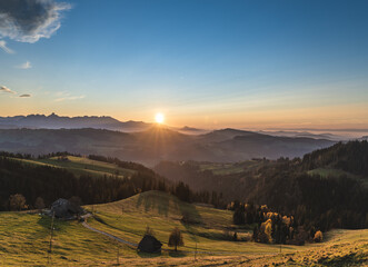 Wall Mural - overview swiss landscape with hills forests mountains in warm color during sunset or sunrise and epi