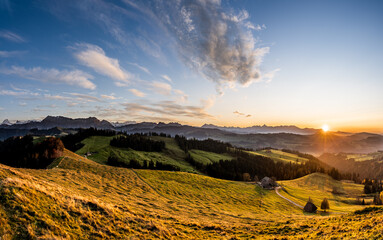 Wall Mural - overview swiss landscape with hills forests mountains in warm color during sunset or sunrise and epi