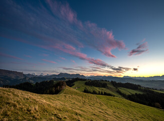 Wall Mural - overview swiss landscape with hills forests mountains in warm color during sunset or sunrise and epi