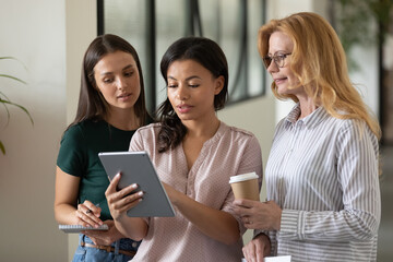 Canvas Print - Informal counseling. Focused young biracial woman office employee consulting helping assisting female colleagues at break time, showing decision proposal on gadget screen, filling in electronic form