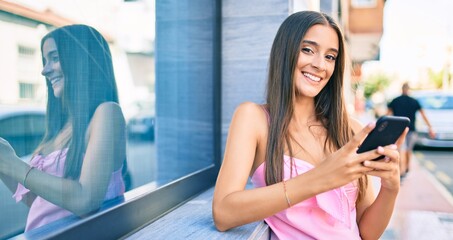 Wall Mural - Young hispanic woman using smartphone leaning on the wall at street of city.