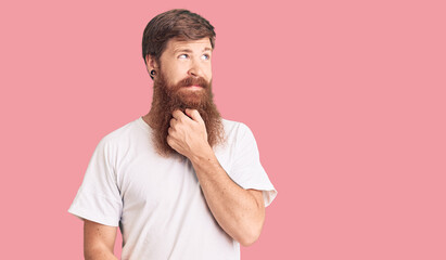 Wall Mural - Handsome young red head man with long beard wearing casual white tshirt with hand on chin thinking about question, pensive expression. smiling with thoughtful face. doubt concept.