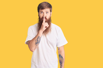 Sticker - Handsome young red head man with long beard wearing casual white tshirt asking to be quiet with finger on lips. silence and secret concept.