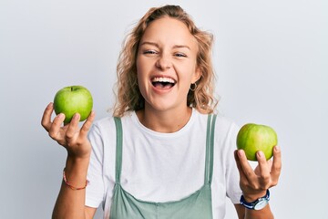 Wall Mural - Beautiful caucasian woman holding green apples smiling and laughing hard out loud because funny crazy joke.