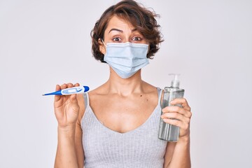 Sticker - Young hispanic woman wearing medical mask, hand sanitizer gel and thermometer puffing cheeks with funny face. mouth inflated with air, catching air.