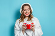 © Evgenia - Beautiful young caucasian woman with red lipstick wearing a white faux fur coat and fur ears smiling and holding a red gift box isolated on winter blue studio background