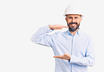 Canvas Print - Young handsome man wearing architect hardhat gesturing with hands showing big and large size sign, measure symbol. smiling looking at the camera. measuring concept.