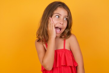 Wall Mural - Caucasian young girl standing against yellow background excited looking to the side hand on face. Advertisement and amazement concept.