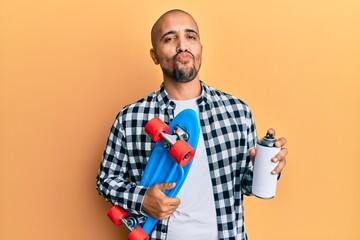 Sticker - Hispanic adult skater man holding skate and graffiti spray looking at the camera blowing a kiss being lovely and sexy. love expression.