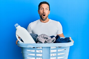 Sticker - Young handsome man holding laundry basket and detergent bottle afraid and shocked with surprise and amazed expression, fear and excited face.