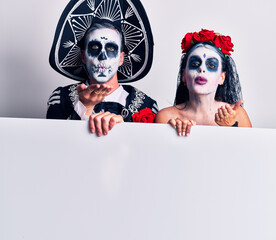 Poster - Young couple wearing mexican day of the dead costume holding blank empty banner looking at the camera blowing a kiss with hand on air being lovely and sexy. love expression.