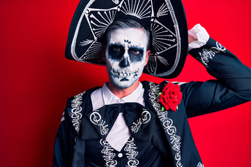 Canvas Print - Young man wearing mexican day of the dead costume over red confuse and wonder about question. uncertain with doubt, thinking with hand on head. pensive concept.