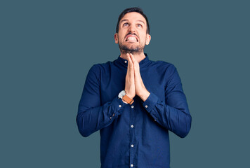 Poster - Young handsome man wearing casual shirt begging and praying with hands together with hope expression on face very emotional and worried. begging.