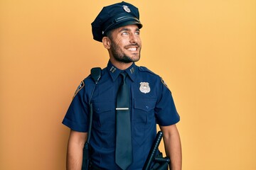 Wall Mural - Handsome hispanic man wearing police uniform looking away to side with smile on face, natural expression. laughing confident.