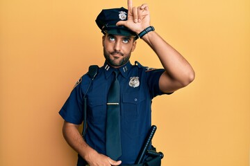 Wall Mural - Handsome hispanic man wearing police uniform making fun of people with fingers on forehead doing loser gesture mocking and insulting.