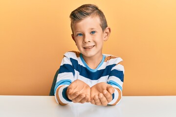 Poster - Adorable caucasian kid wearing casual clothes sitting on the table smiling with hands palms together receiving or giving gesture. hold and protection