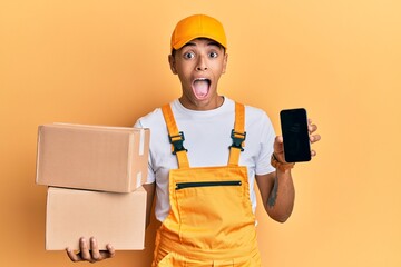 Sticker - Young handsome african american man holding delivery package and showing smartphone screen celebrating crazy and amazed for success with open eyes screaming excited.