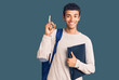 © Krakenimages.com - Young african amercian man wearing student backpack holding binder surprised with an idea or question pointing finger with happy face, number one