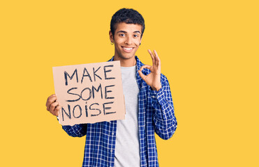 Wall Mural - Young african amercian man holding make some noise banner doing ok sign with fingers, smiling friendly gesturing excellent symbol