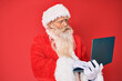 © Krakenimages.com - Old senior man with grey hair and long beard wearing santa claus costume using laptop in shock face, looking skeptical and sarcastic, surprised with open mouth